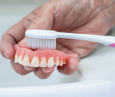 someone cleaning dentures with a toothbrush
