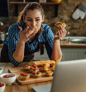 Woman enjoying snack in kitchen with laptop
