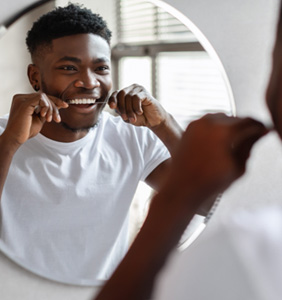 Man smiling while flossing in bathroom