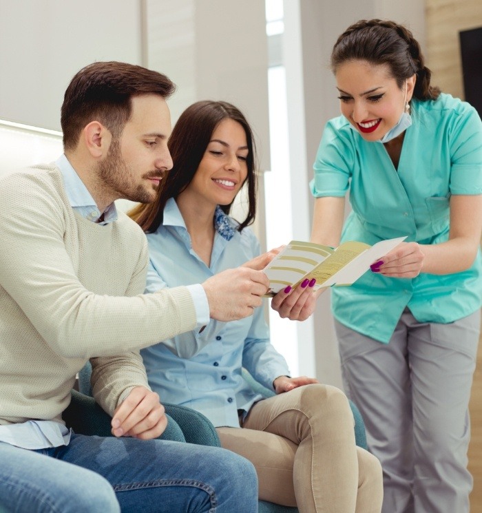 Dental team member showing couple pamphlet about the cost of dental implants