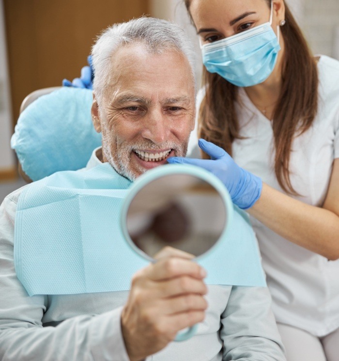 Senior dental patient looking at his smile in mirror