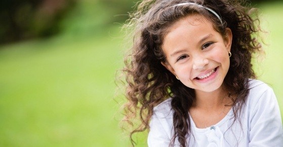 Young girl with curly brown hair grinning outdoors