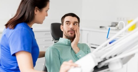 Man in dental chair holding his cheek in pain