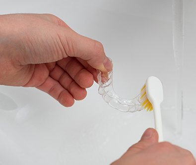 A person cleaning their aligners with water