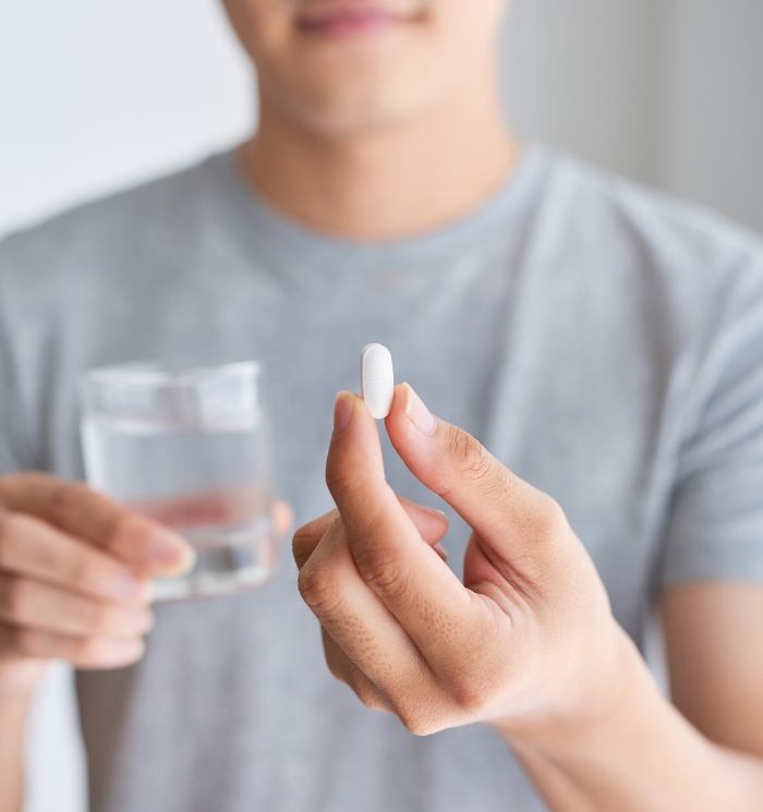 Person holding a pill and a glass of water