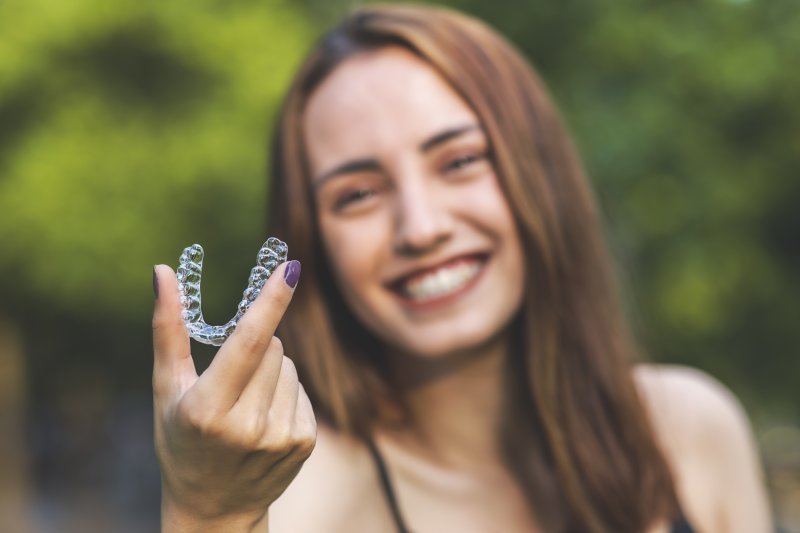 person smiling and holding Invisalign tray